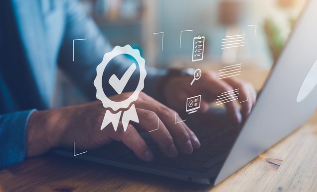 Hände eines Mannes an einem Notebook und davor illustrative Prämien-Zeichen